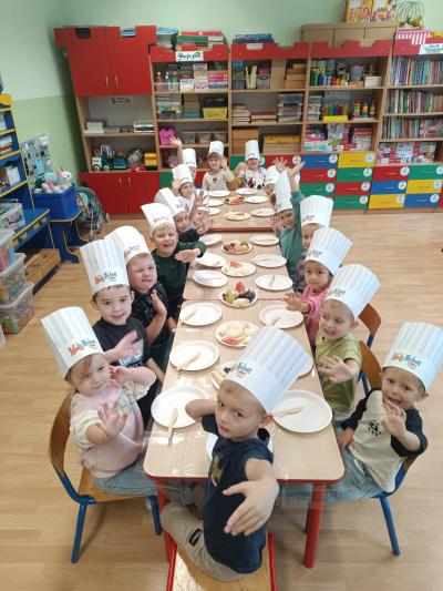 Przedszkolaki kroją owoce na talerzykach przy stole.