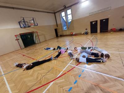 Dzieci tworzą latawce z ciał na podłodze sali gimnastycznej.