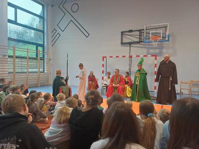 Uczniowie siedzą. Na scenie stoją m.in.: biskup, zakonnik, Dobrawa, Mieszko I, Bolesław Chrobry.