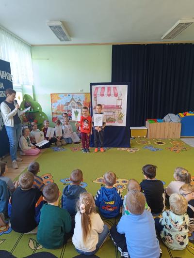 Uczniowie stoją i trzymają w rękach ilustracje z warzywami.