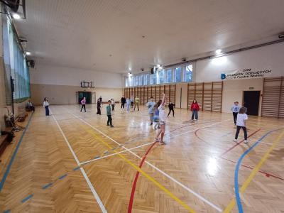 Uczniowie grają w piłkę na hali sportowej.