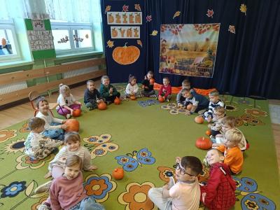 Dzieci siedzą w kole na dywanie i mają przed sobą dynie.