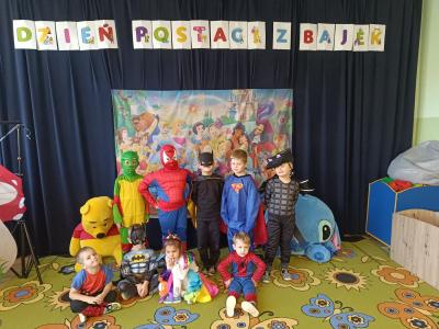 Przedszkolaki przebrane za postacie z bajek stoją na tle postaci z bajek Disney'a.