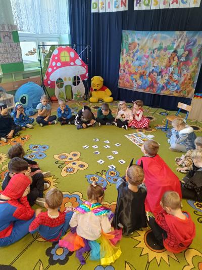 Przedszkolaki przebrane za postacie z bajek siedzą w kole, na dywanie.