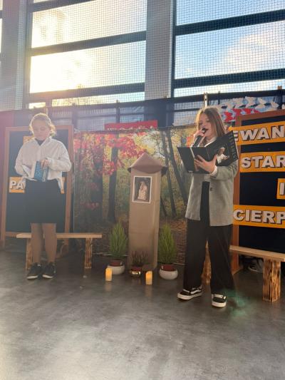 Uczennica stoją na scenie po obu stronach kapliczki z Panem Jezusem Frasobliwym i czytają teksty.