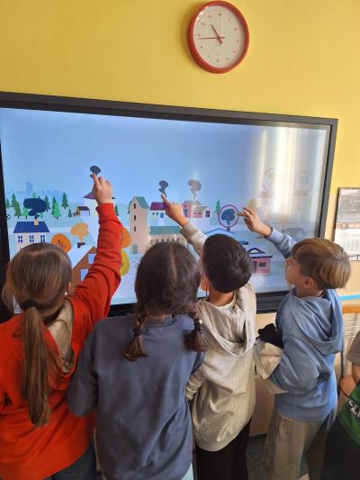 Uczniowie grają w grę edukacyjną na tablicy multimedialnej.