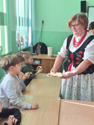 Pani z Koła Gospodyń Wiejskich częstuje uczniów chlebem posmarowanym swojskim masłem.