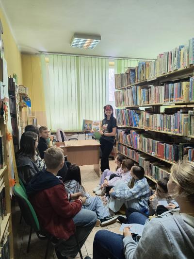 Uczniowie siedzą w bibliotece i słuchają bajki czytanej przez panią bibliotekarkę.