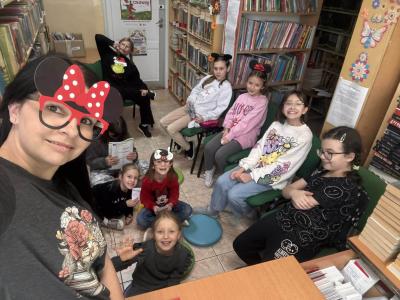 Uczniowie siedzą w bibliotece i słuchają bajki czytanej przez panią bibliotekarkę.