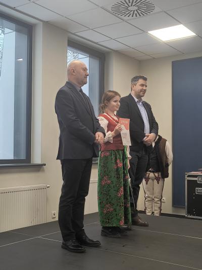 Uczennica trzyma w dłoniach dyplom i pozuje wraz z jury do zdjęcia.