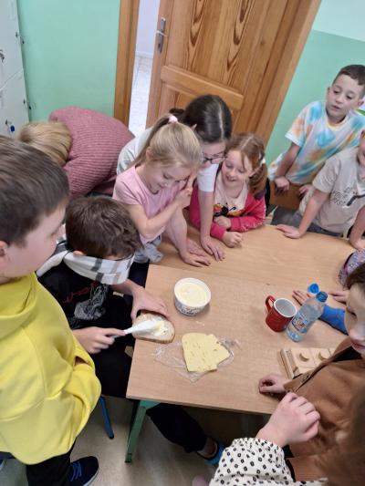 Uczeń z zawiązanymi oczami smaruje kanapkę masłem.