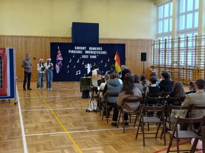 Uczennice w czapkach mikołajkowych na głowie witają jury oraz uczestników konkursu i ich opiekunów.