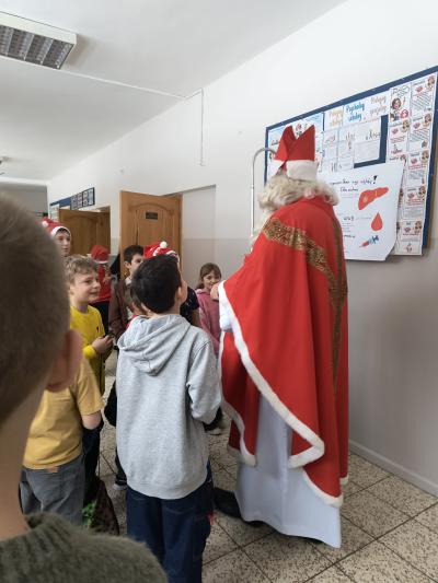 Św. Mikołaj rozdaje dzieciom cukierki na szkolnym korytarzu.