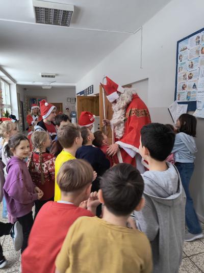 Św. Mikołaj rozdaje dzieciom cukierki na szkolnym korytarzu.