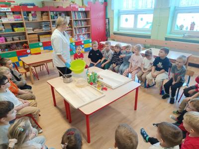 Dzieci siedzą w kole na krzesłach i słuchają pani Kasi, jak się robi pierniczki.