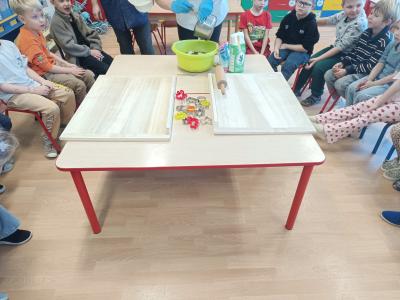 Dzieci siedzą w kole, na krzesłach i przyglądają się, jak się robi ciasto na pierniczki.