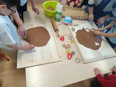 Dzieci wykrawają foremkami pierniczki w cieście.