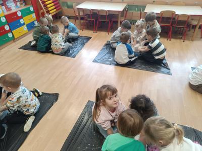 Przedszkolaki siedzą w grupkach na podłodze, a w miskach znajduje się piankolina.