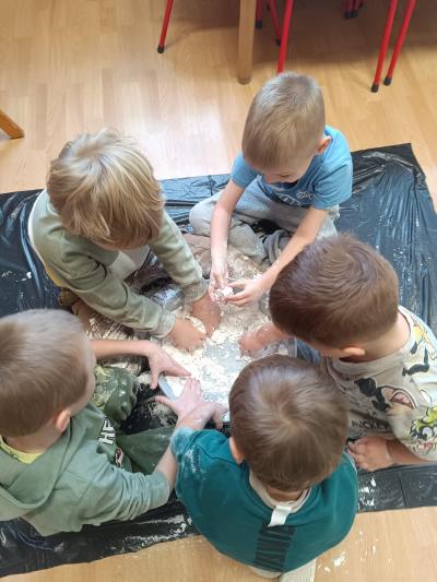 Przedszkolaki siedzą w grupkach na podłodze, a w miskach znajduje się piankolina.