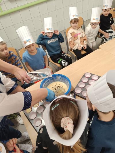 Dzieci przyglądają się, jak kucharka robi ciasto.