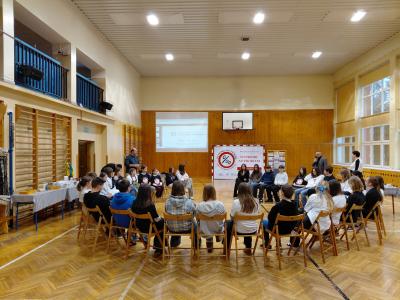 Uczniowie siedzą w kole na krzesłach, na sali gimnastycznej.