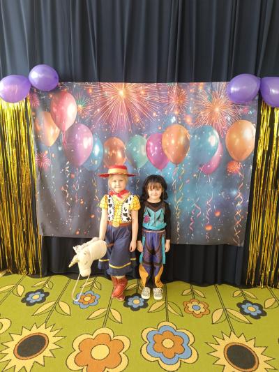 Dzieci przebrane za postacie z gier i bajek stoją na karnawałowym tle z balonami.