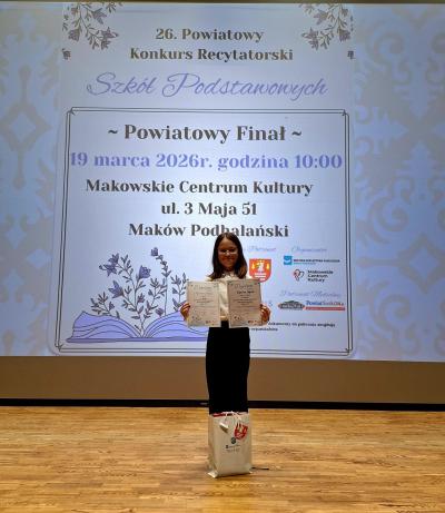 Uczennica stoi na scenie z dyplomami w rękach.