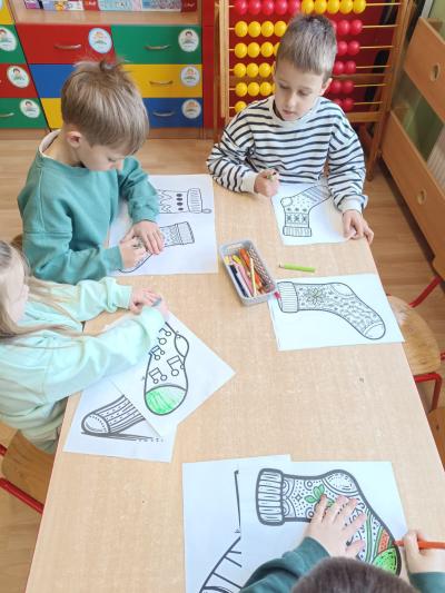 Dzieci kolorują przy stolikach papierowe skarpetki.