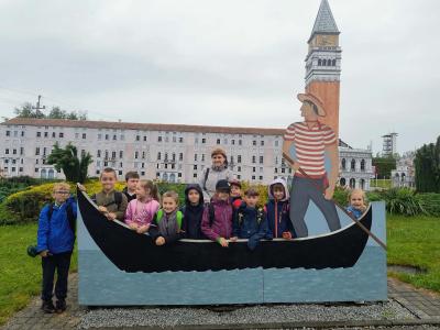 Uczniowie stoją przed miniaturą Pałacu Weneckiego, za atrapą łodzi.