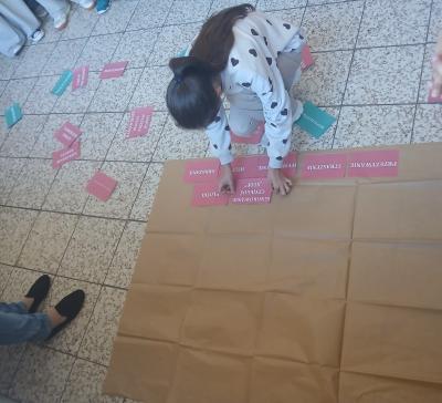 Uczennica przykleja cegły z papieru do szarego papieru.