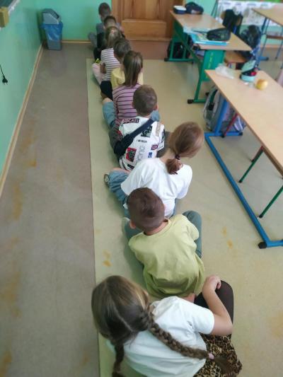 Dzieci siedzą na podłodze jeden za drugim.